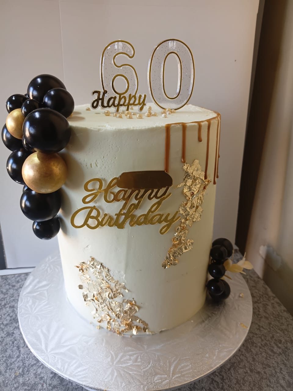 White cake with black and gold balloon cluster and gold leaf for a 60th birthday
